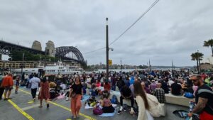 View of Campbells Cove, large crowd of people camped out, waiting for New Year's Eve fireworks. Harbour Bridge visible, Opera House barely