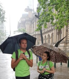 Two tour guides standing in Sydney Square near Town Hall in the rain with umbrellas