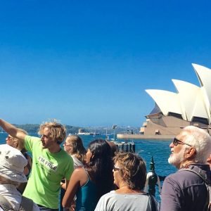 An I'm Free Tours guide, wearing a bright green T-shirt, with a tour group in front of the Sydney Opera House.